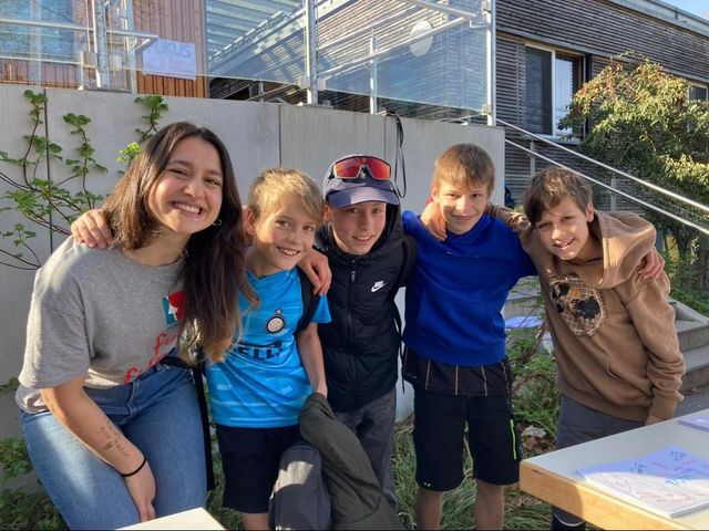 Eine Frau und ihre vier Kinder lächeln und posieren im Freien, die Arme umeinander geschlungen.