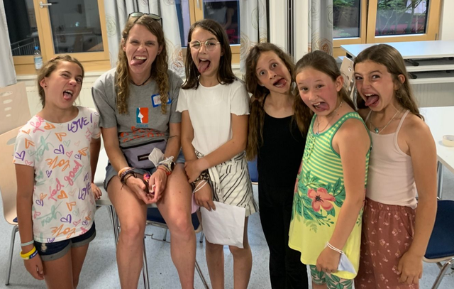 Eine Gruppe von Menschen streckt die Zunge heraus. Drinnen sitzen und stehen sie lächelnd.