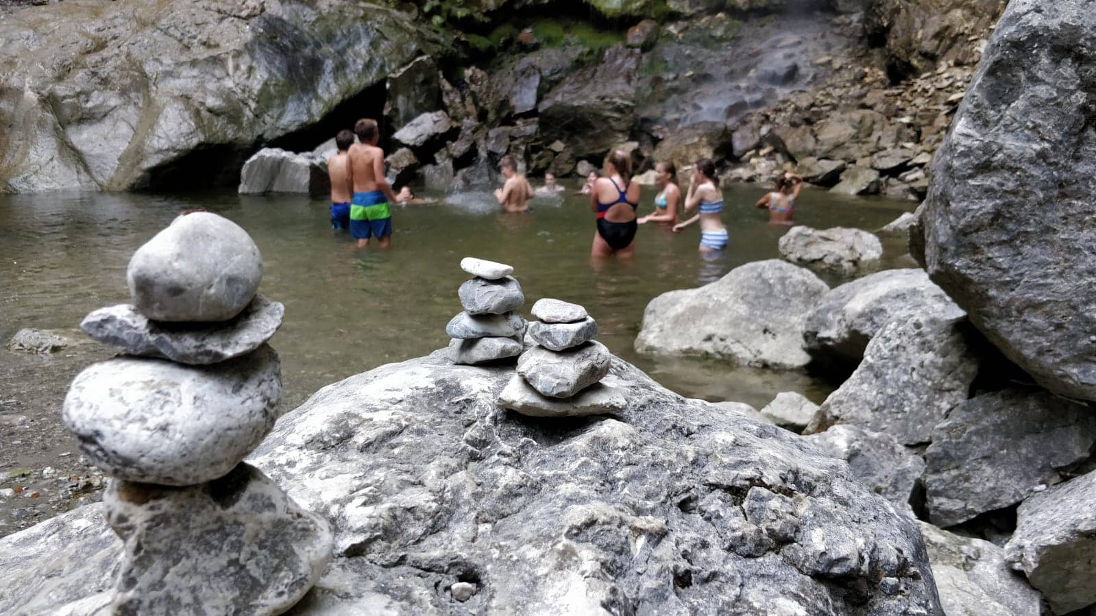 Eine Gruppe von Menschen schwimmt in einem Fluss neben einem Steinhaufen.