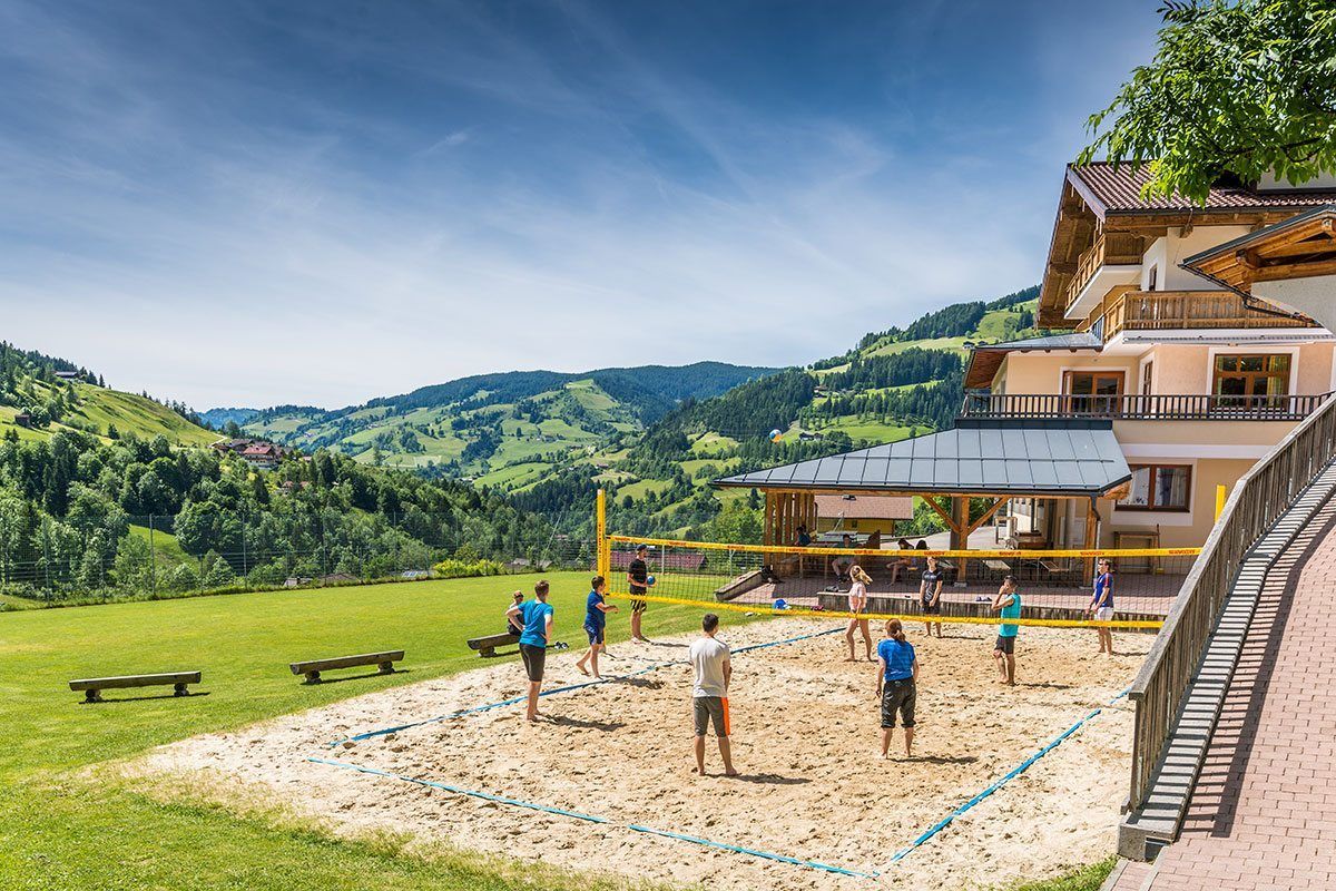 Eine Gruppe von Menschen spielt Volleyball auf einem Sandplatz vor einem Gebäude.