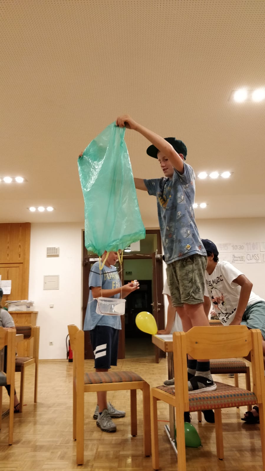 Jungen in einem Zimmer, die ein Spiel mit einer Plastiktüte, Luftballons und Stühlen spielen.