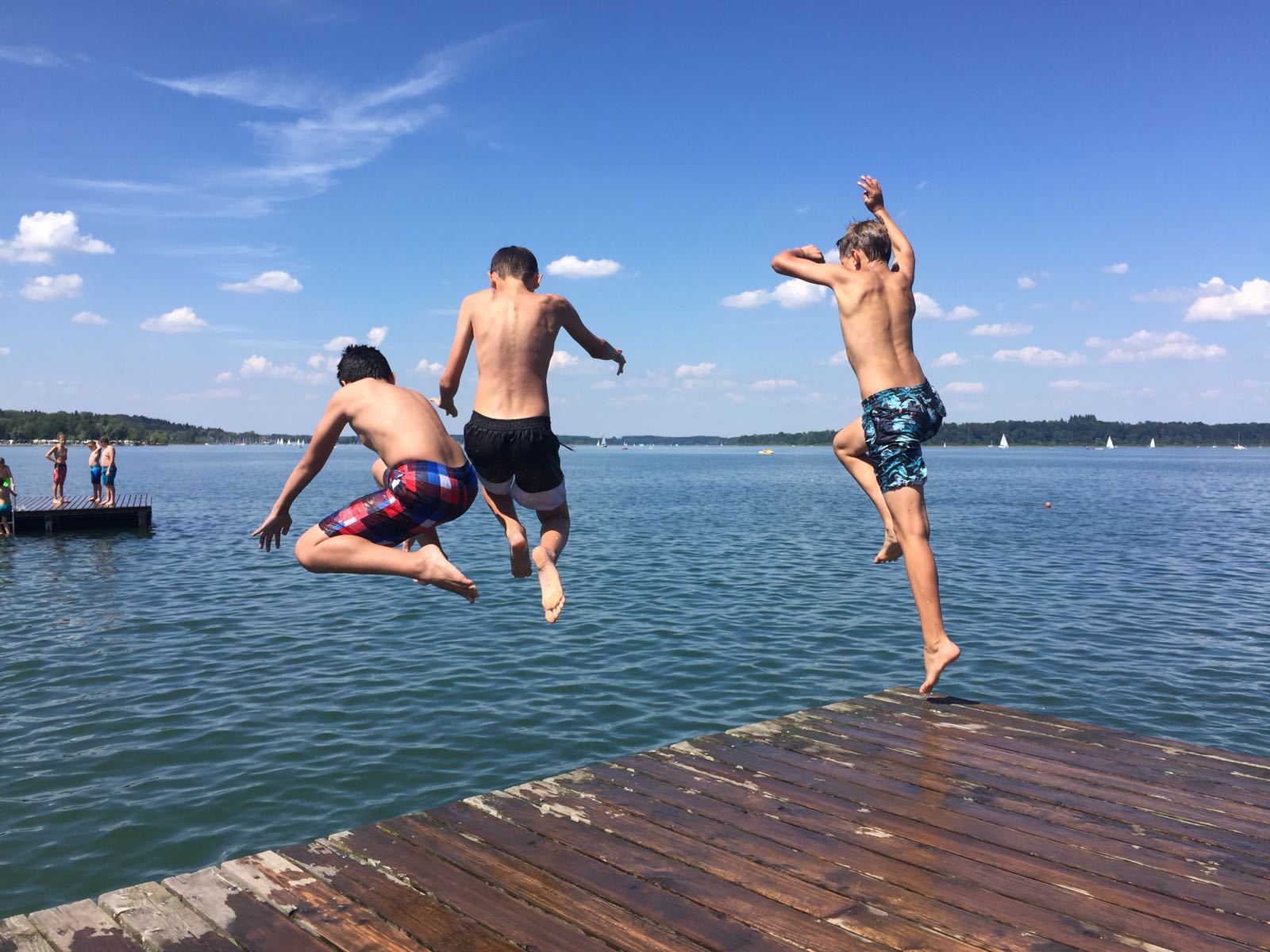 Drei Jungen springen von einem Steg in einen See.