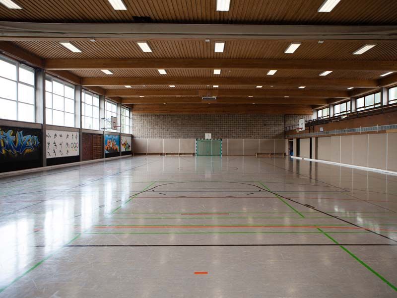 Leere Turnhalle mit Holzdecke, Basketballkörben und markiertem Boden.