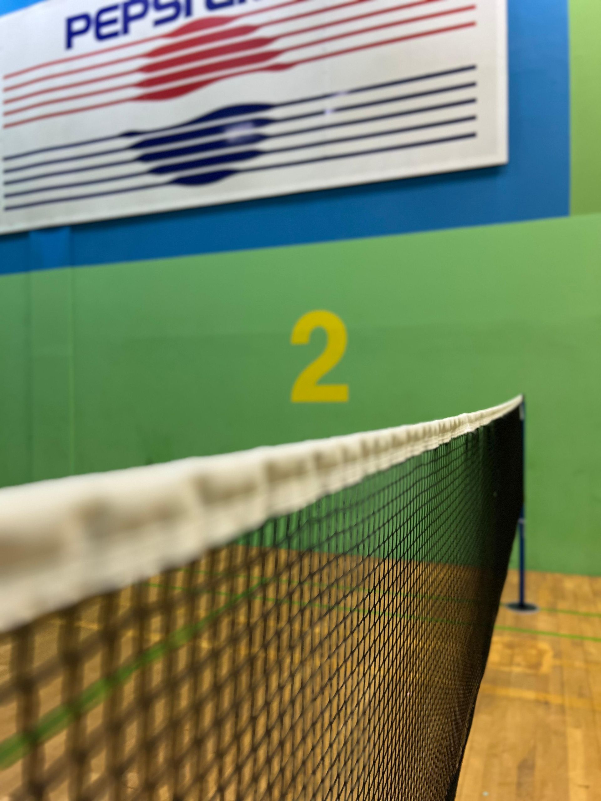 Badmintonnetz mit grünen und blauen Wänden, Pepsi-Logo im Hintergrund und der Zahl 2.