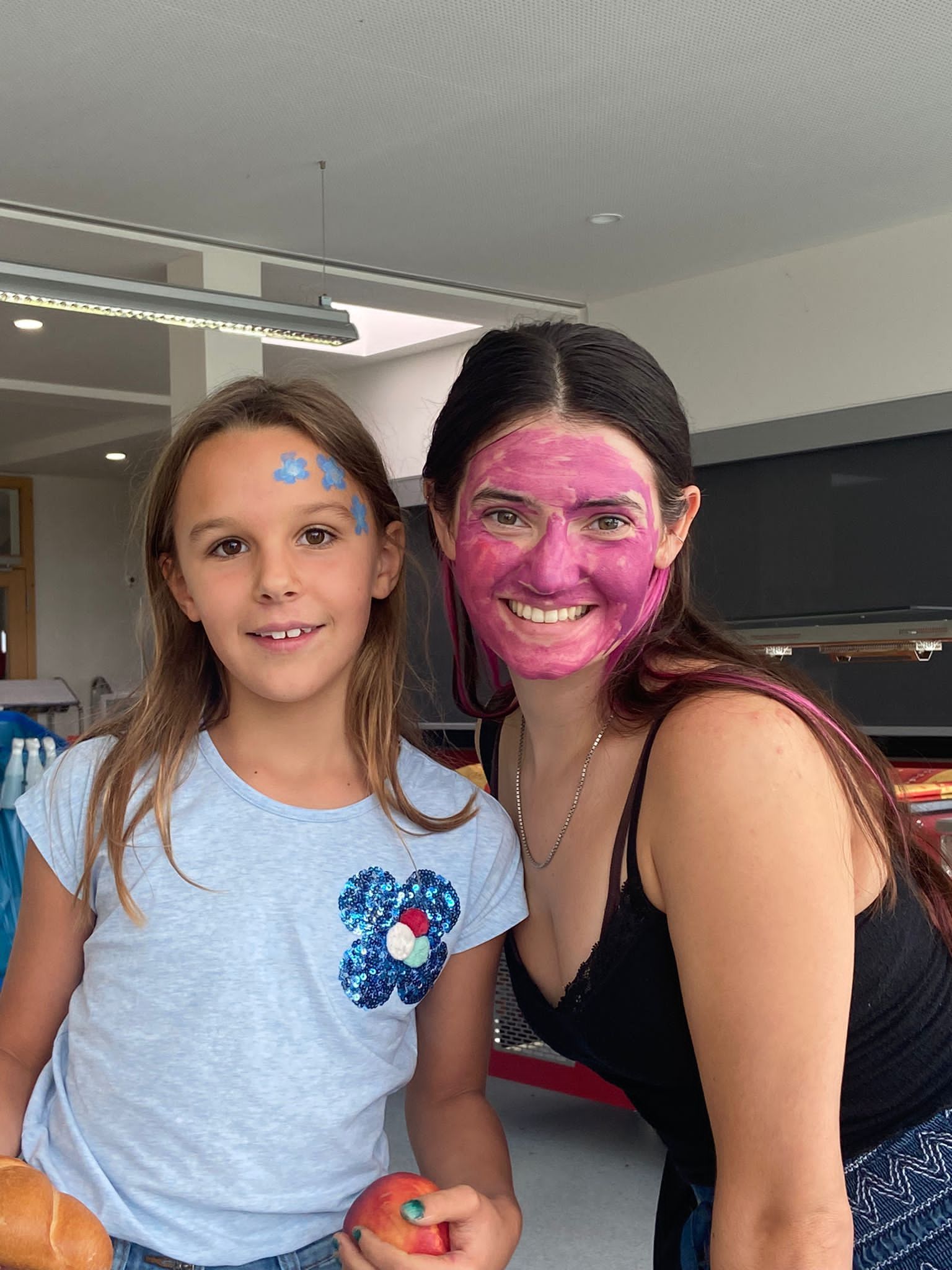 Eine Frau mit einer rosa Maske im Gesicht steht neben einem kleinen Mädchen.