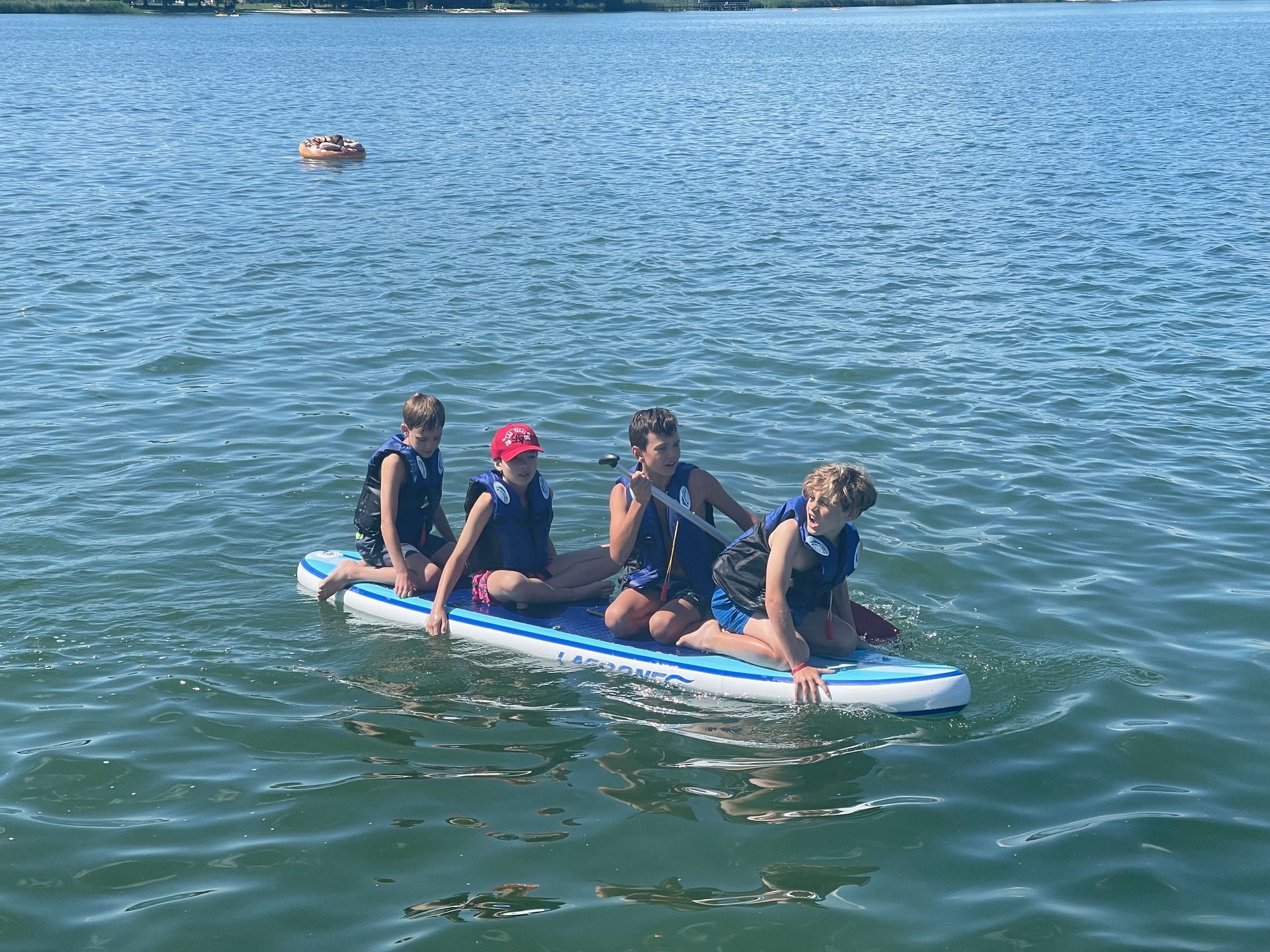 Vier Kinder in Schwimmwesten auf einem Paddleboard in einem Gewässer.