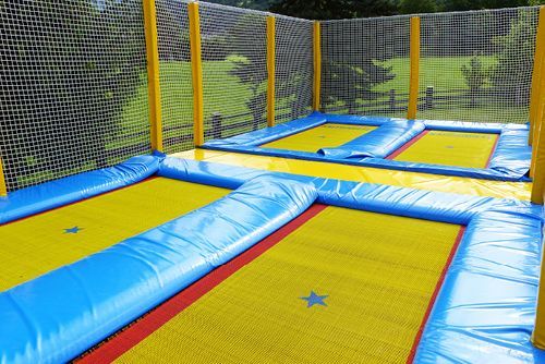 Mehrere gelbe und blaue Trampoline in einem umzäunten Bereich, bereit zum Springen.