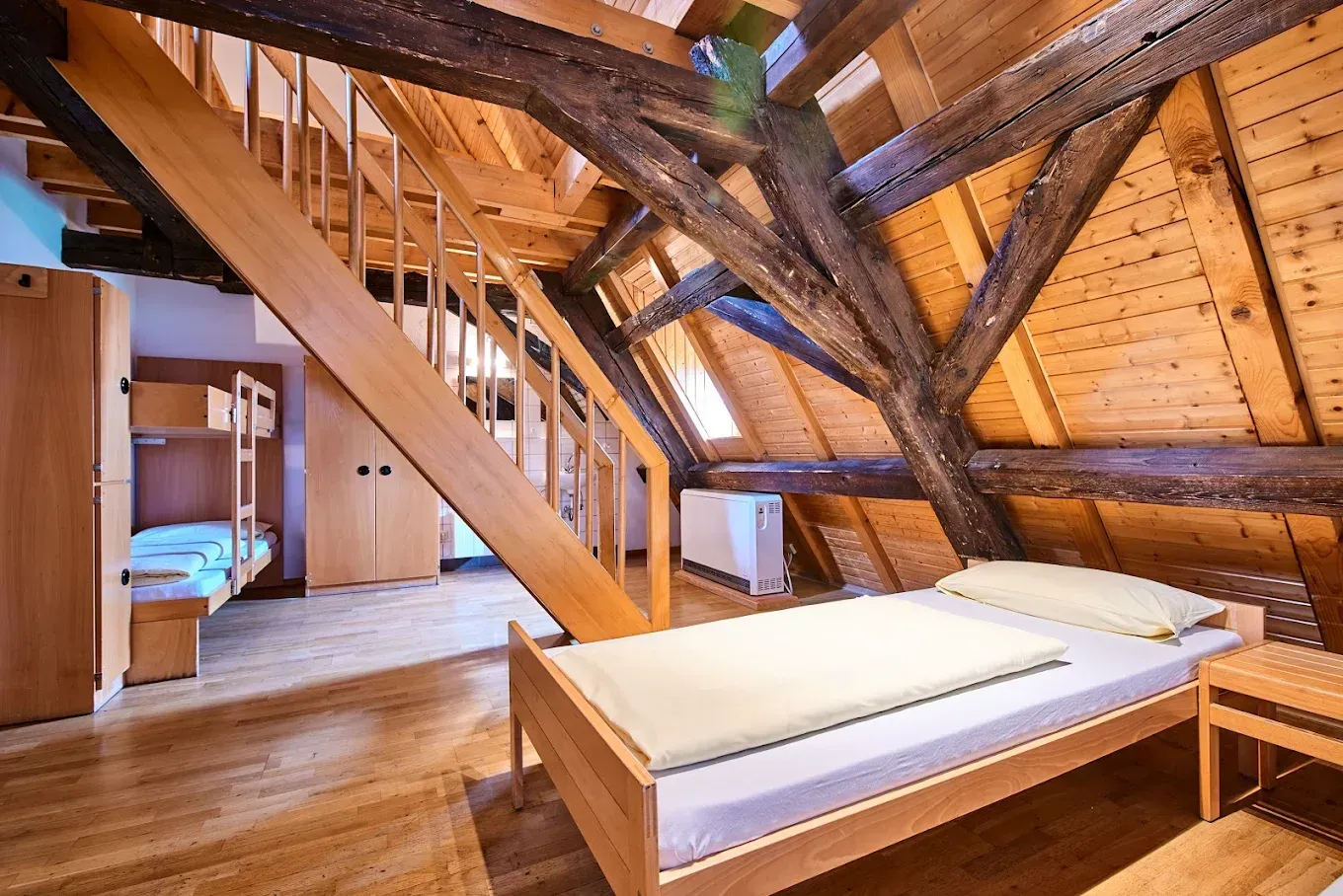 Ein Schlafsaal mit zwei Betten, einem Kleiderschrank, Fenstern mit Vorhängen und einem Schreibtisch.