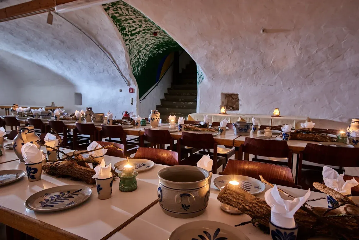 Lange Esstische sind in einem höhlenartigen Raum mit Steinwänden gedeckt, der von Kerzen erleuchtet wird.