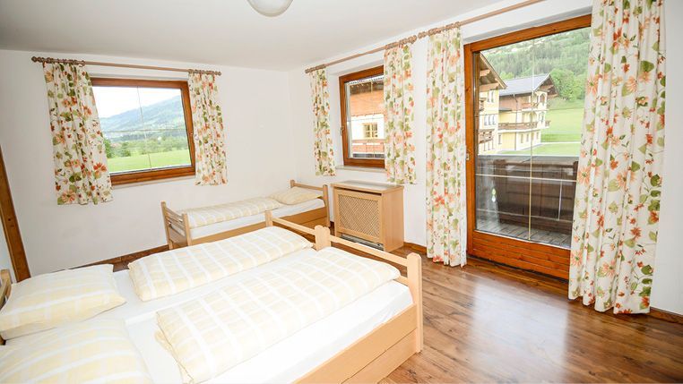 Schlafzimmer mit zwei Einzelbetten, einem Einzelbett und einem Balkon mit Blick auf eine grüne Landschaft.