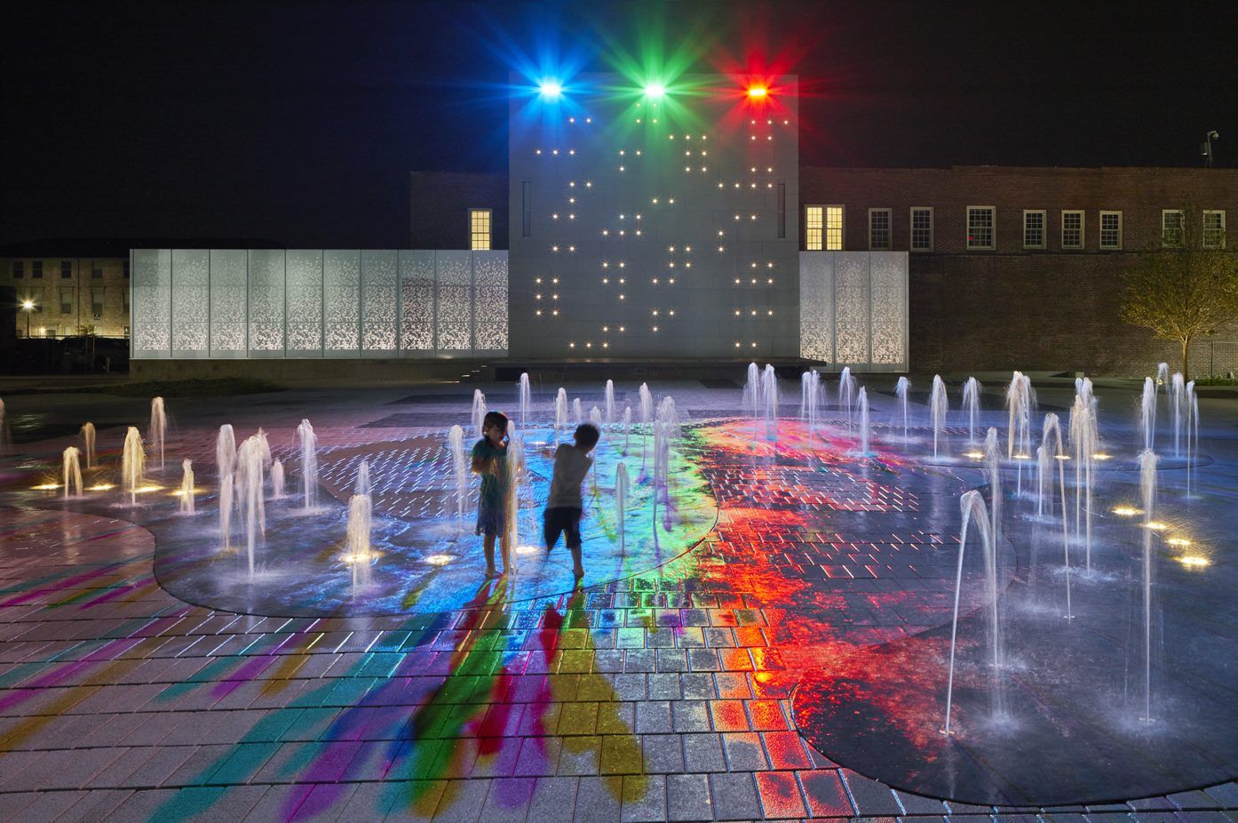 Two children are playing in a fountain at night.