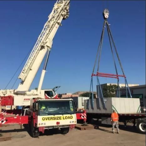 An oversize load truck is being lifted by a crane