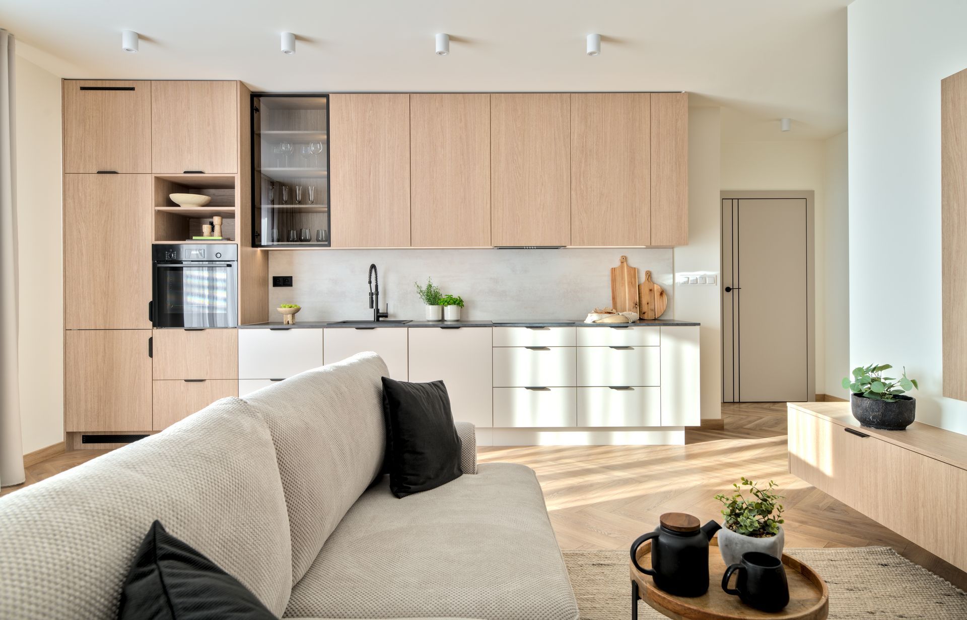 Modern open-plan living room with light wood kitchen cabinets and a beige sofa in the foreground