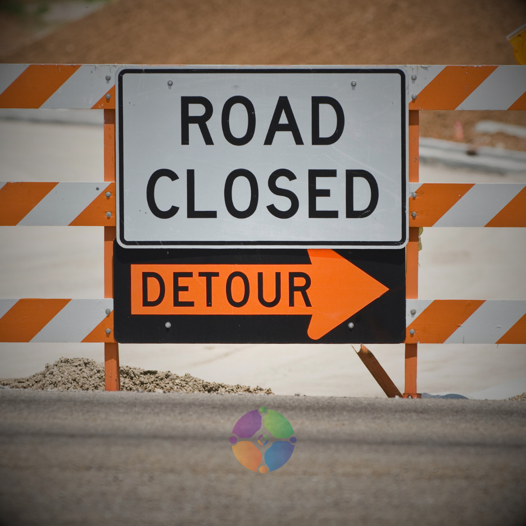 Road closed sign with detour arrow on orange and white barricade.