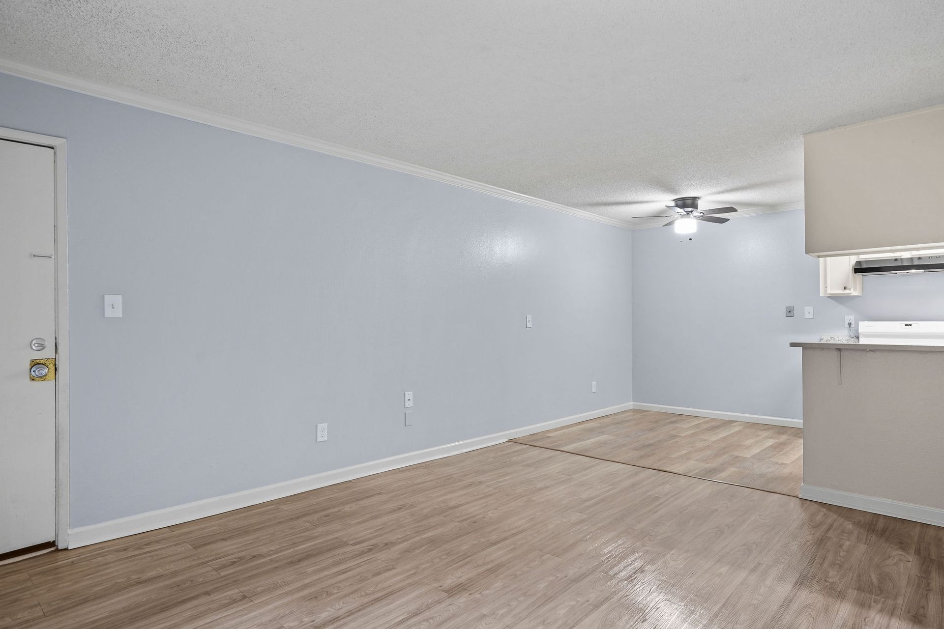 Empty light-blue living room with wood-look flooring, kitchen pass-through, and ceiling fan.