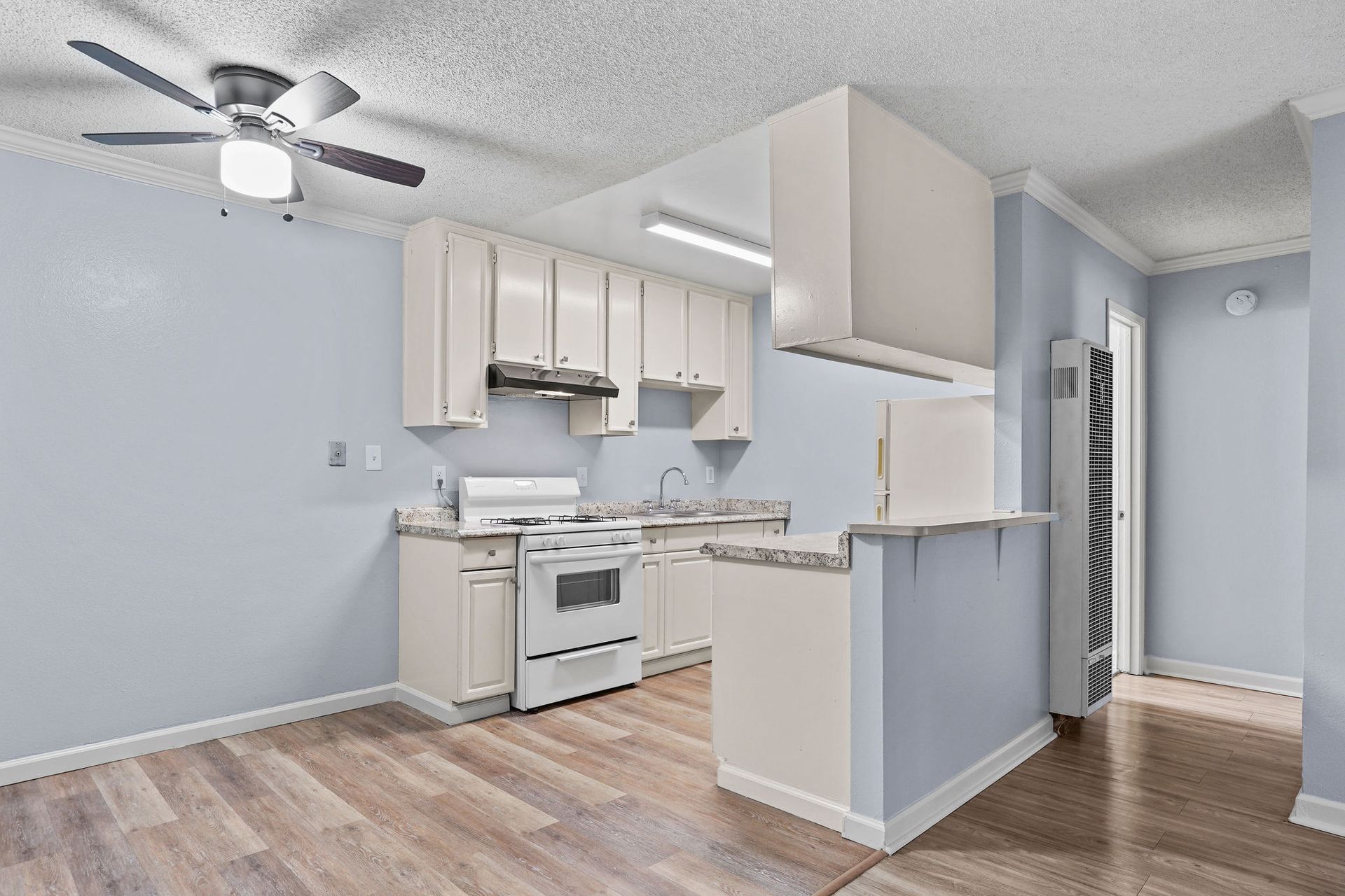 Empty modern kitchen with white cabinets, light wood floors, and a gray wall and ceiling fan