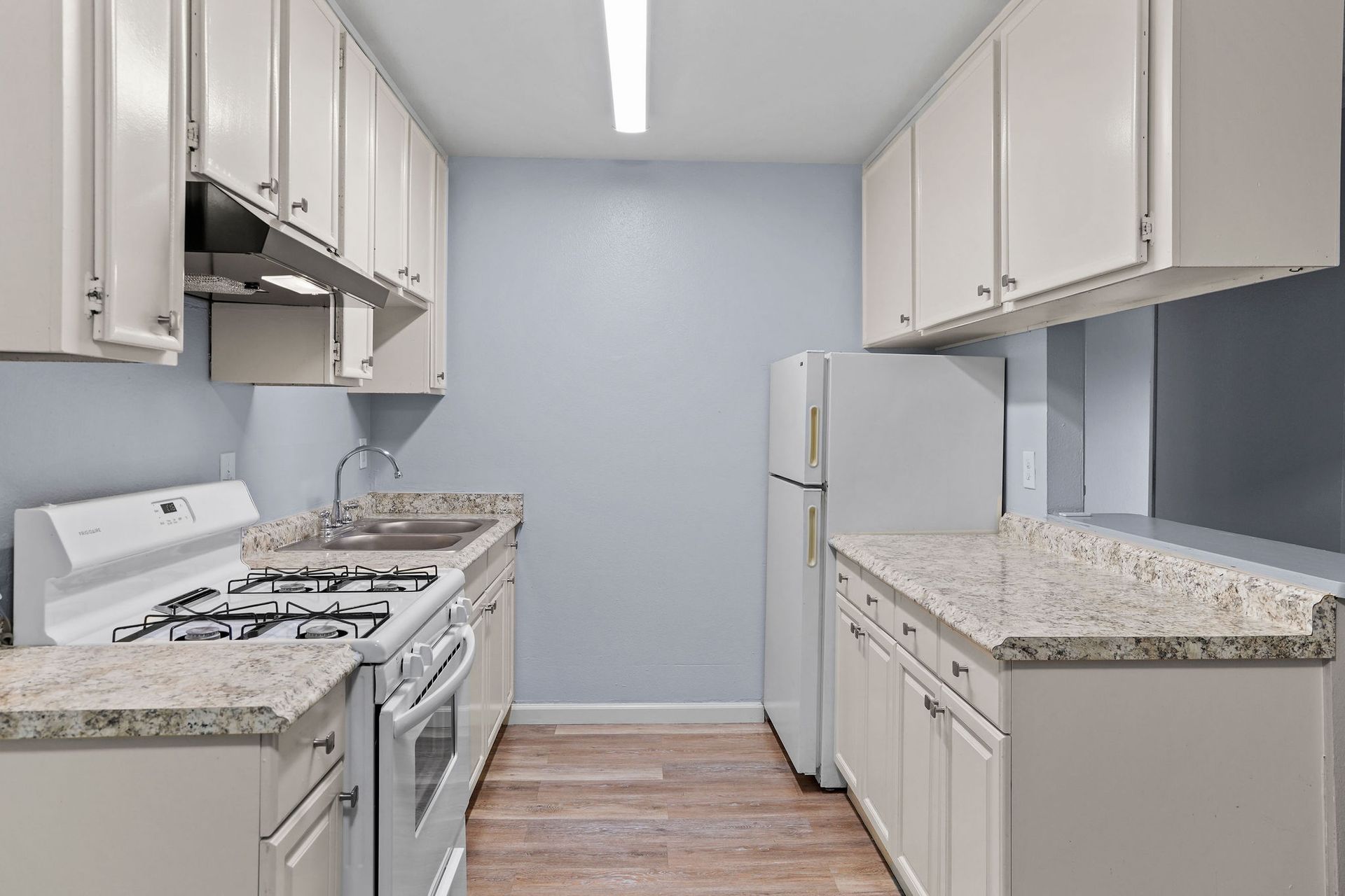 Bright white kitchen with granite counters, white cabinets, gas stove, and refrigerator