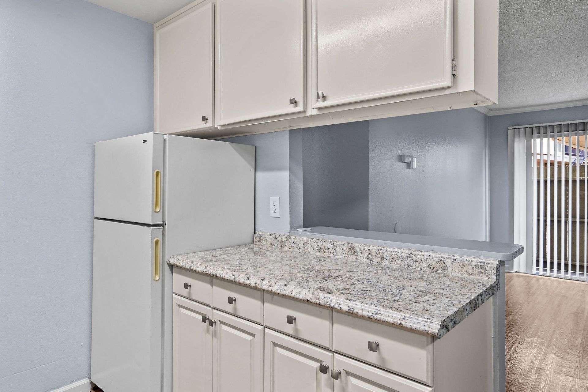 Small kitchen with white cabinets, speckled countertop, and a white refrigerator.