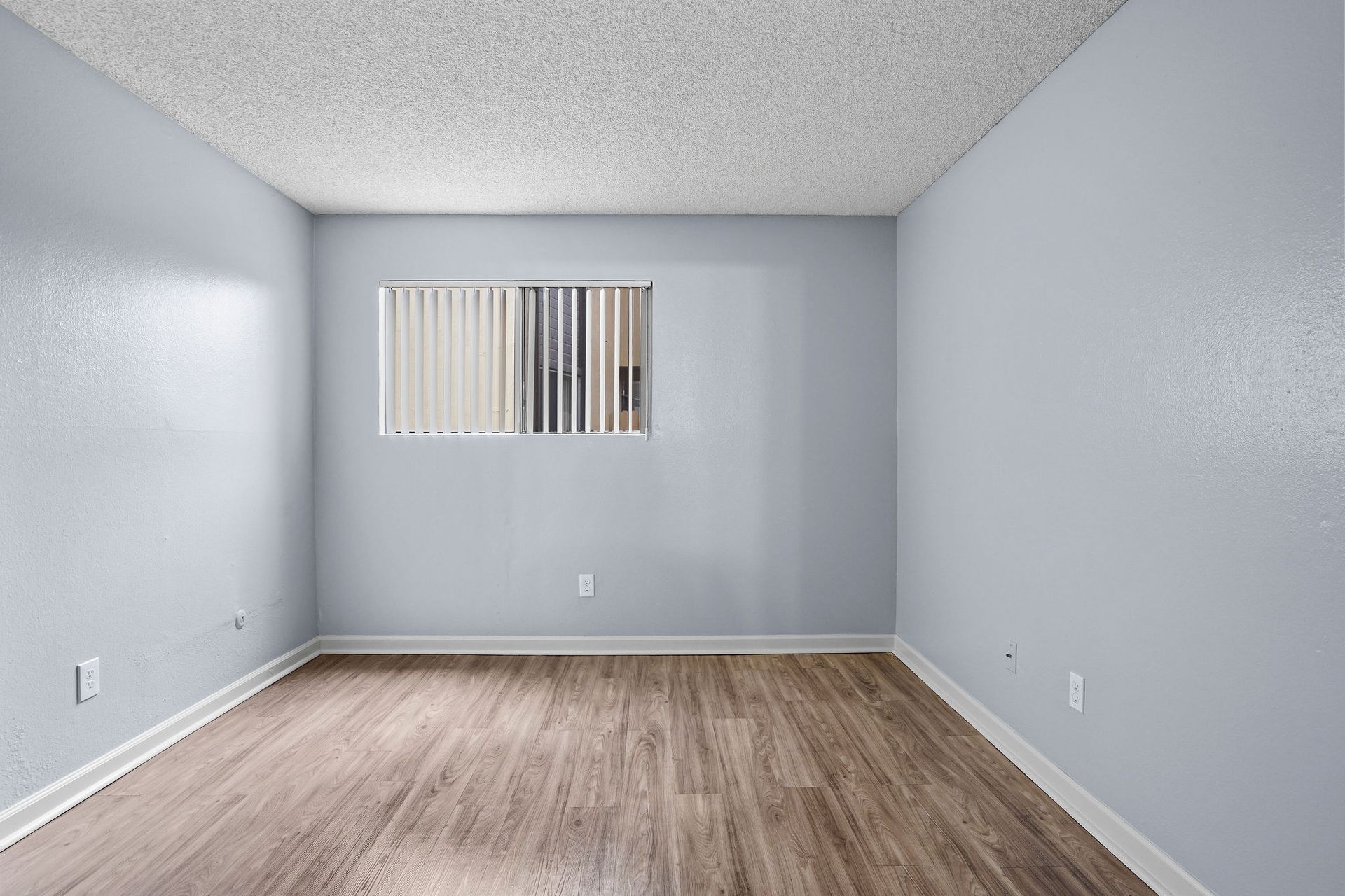 Empty gray room with wood flooring and a small window with vertical blinds