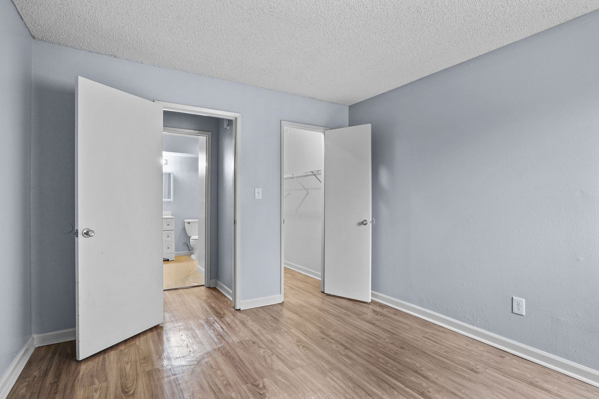 Empty light-blue bedroom with open white doors and wood flooring.