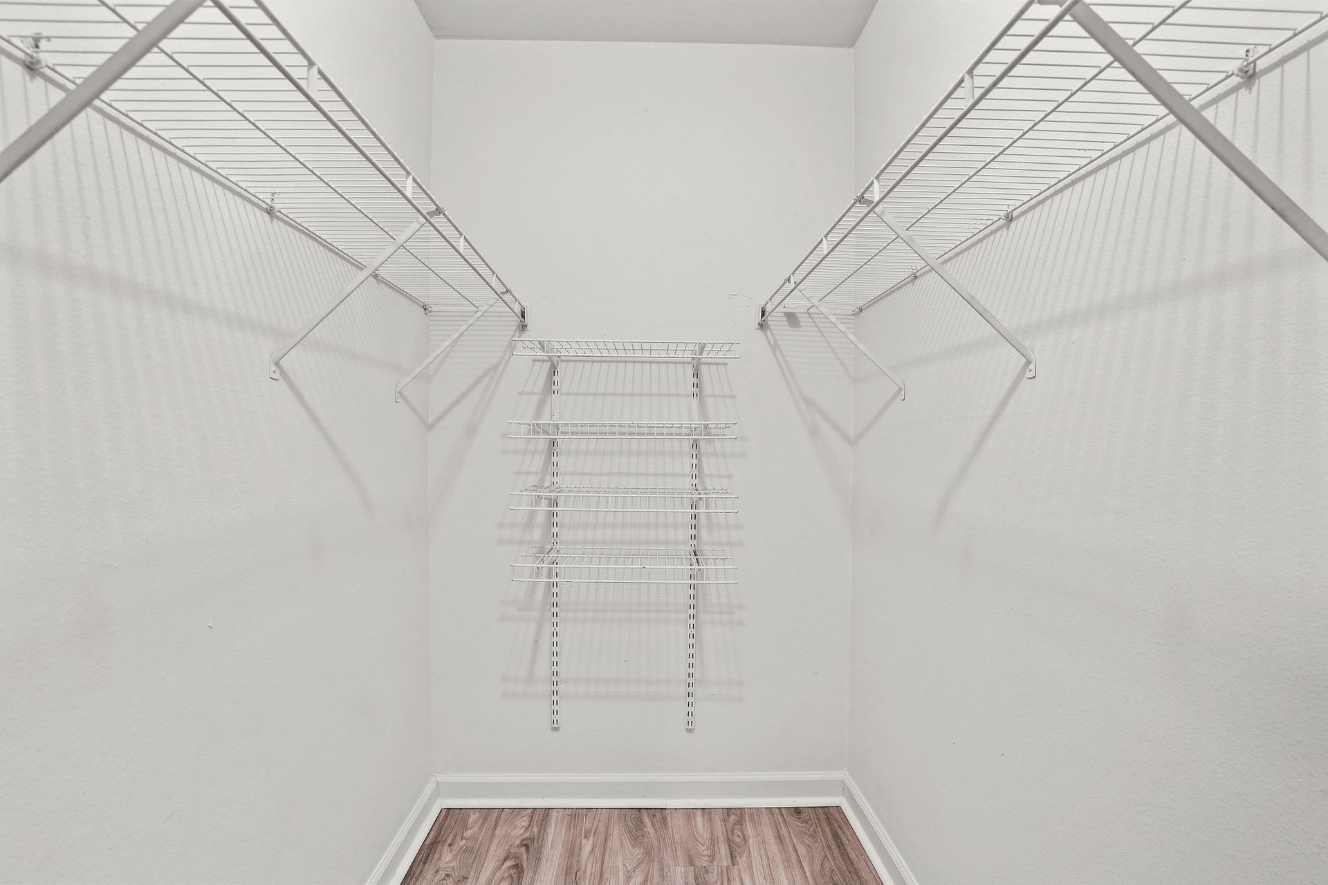 Empty white walk-in closet with wire shelving on both sides and at the back, and carpeted floor.