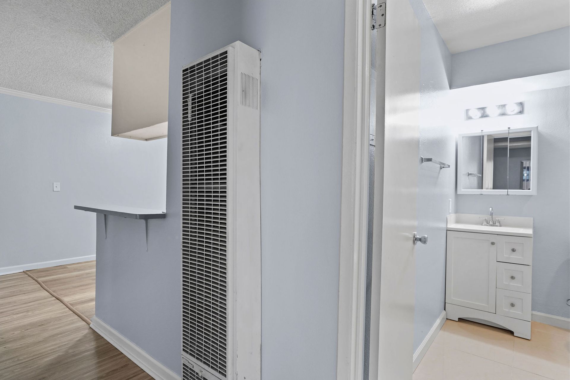 Bright apartment hallway beside a bathroom vanity and white louvered wall heater