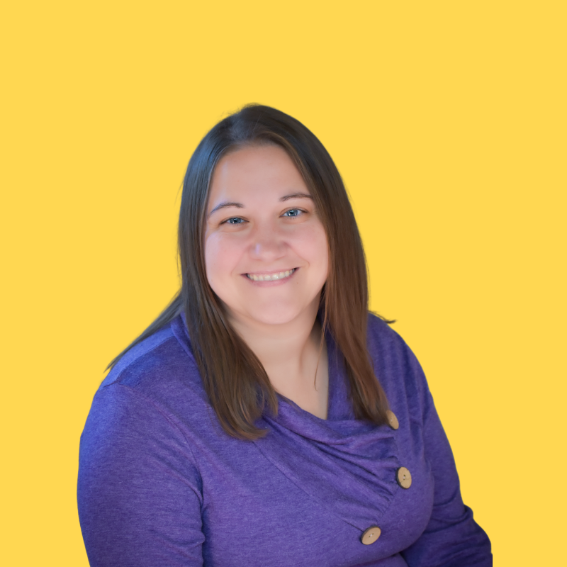 Woman with brown hair and blue eyes smiles, wearing purple sweater, yellow background.