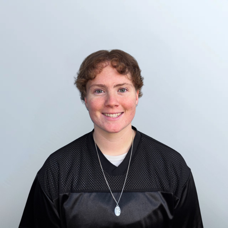 Woman wearing a black mesh jersey, smiling with a necklace, against a gray background.