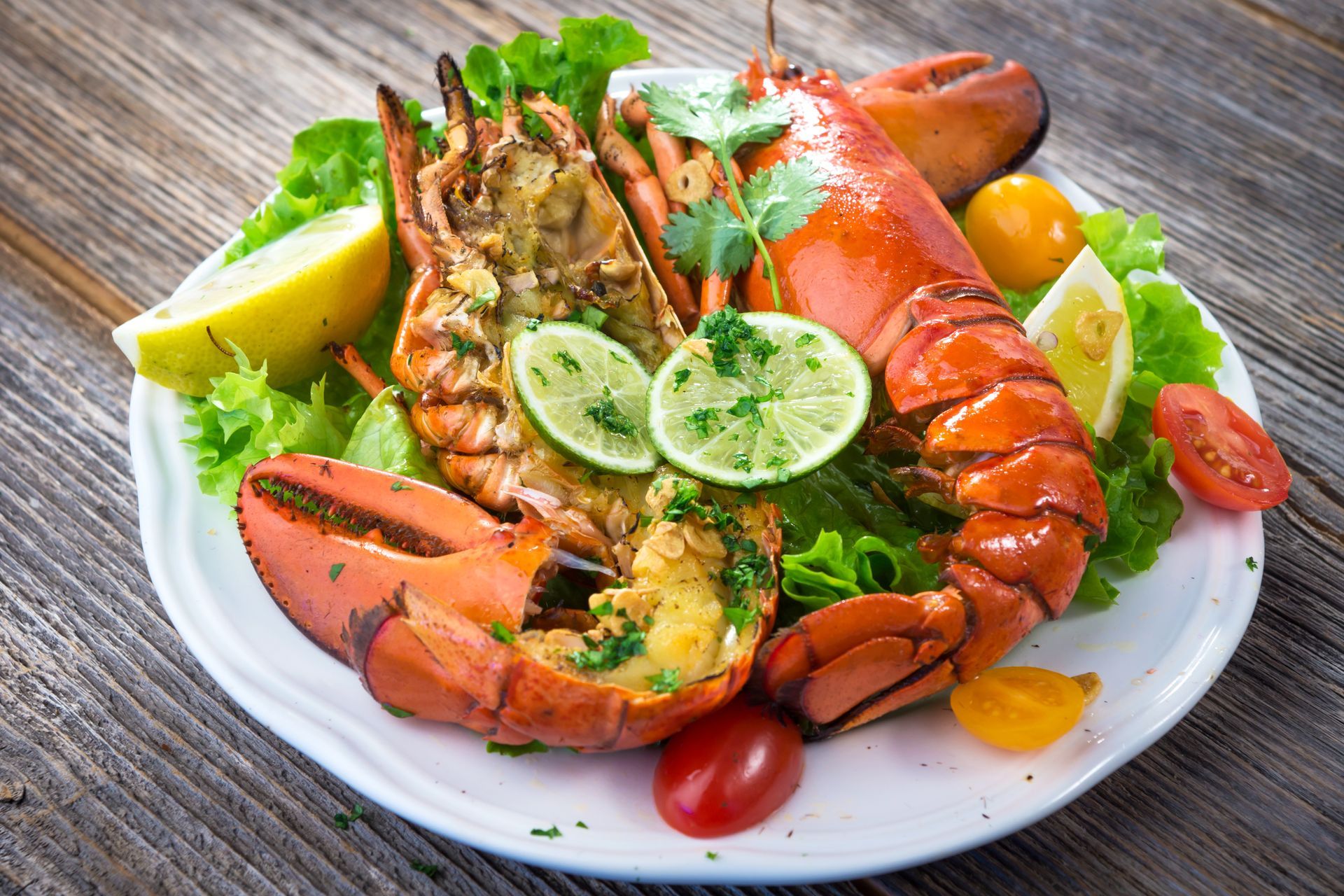 A white plate topped with lobster , lettuce , tomatoes and lemon slices on a wooden table.