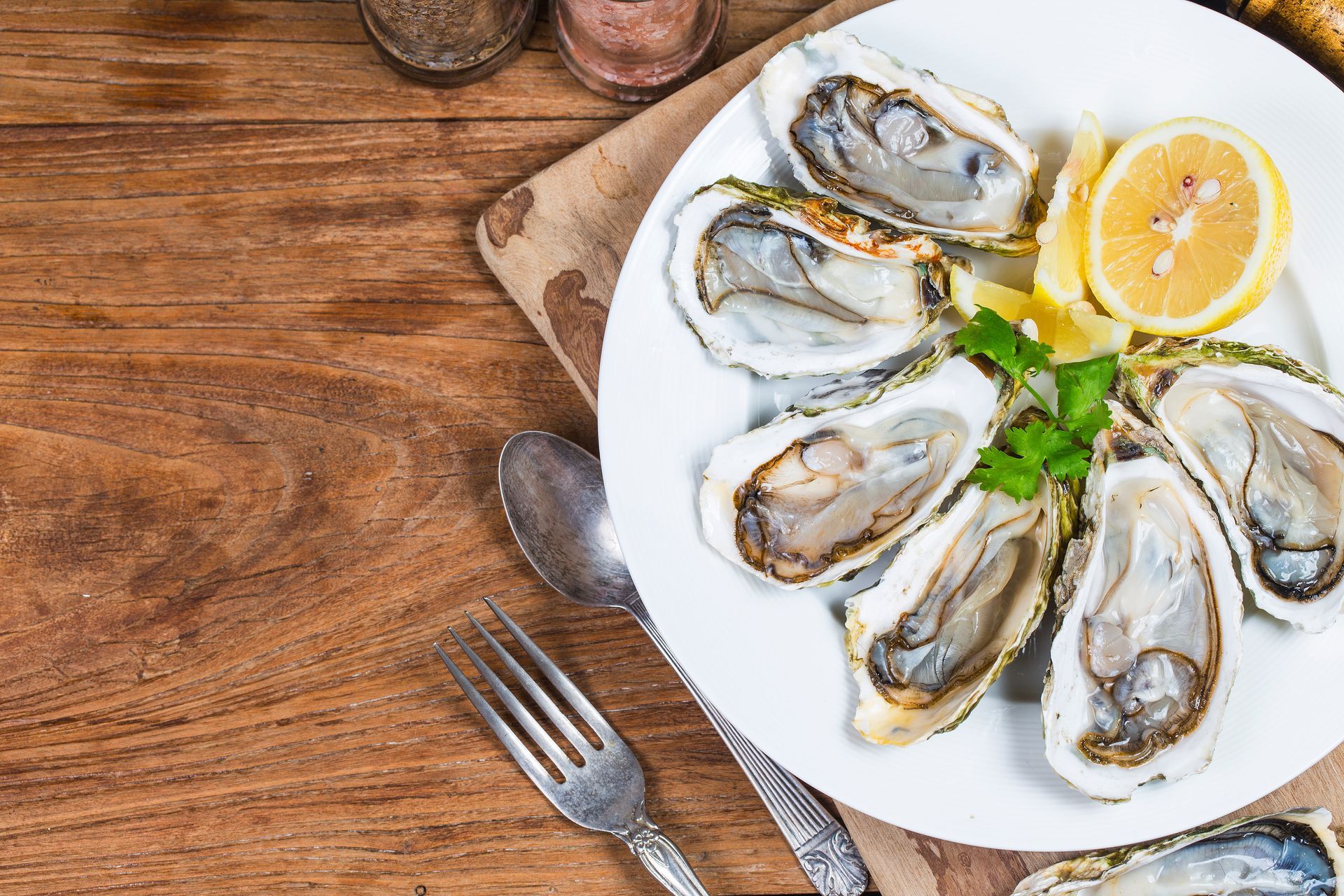 A plate of oysters with lemon and parsley on a wooden table.