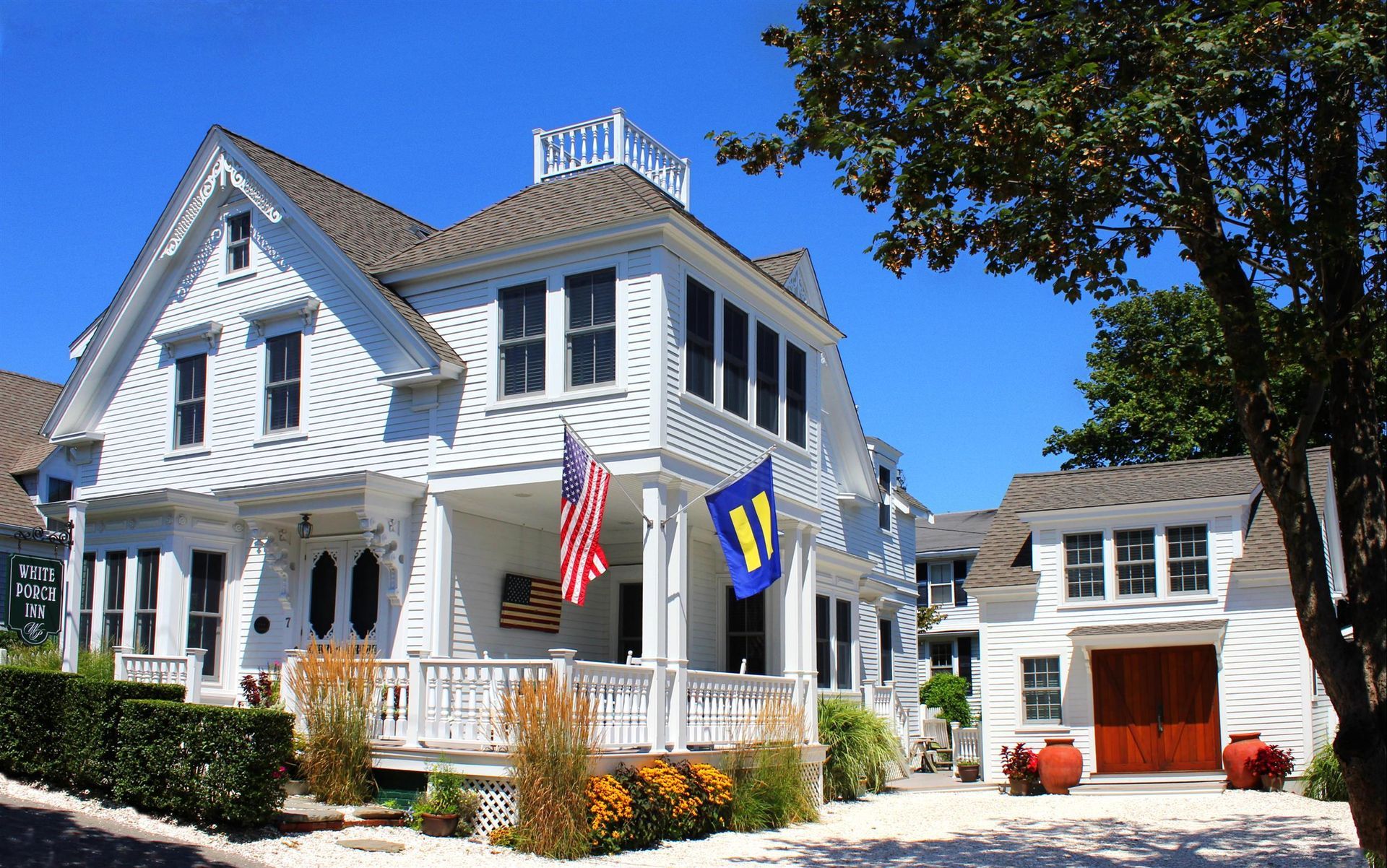 Exterior picture  of the main house with front porch and carriage house with garden in front of it.