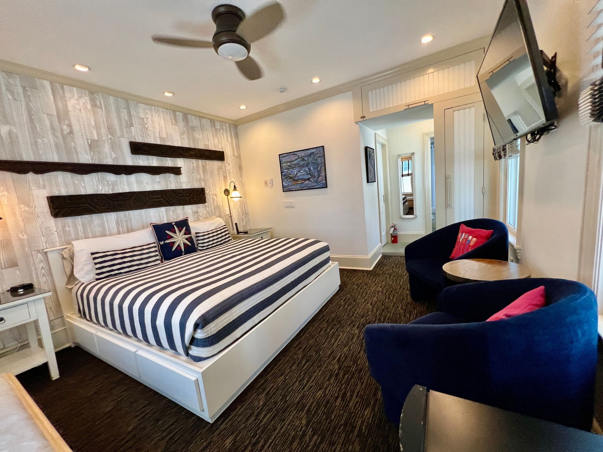A bedroom with a king size bed , two chairs , a television and a ceiling fan.