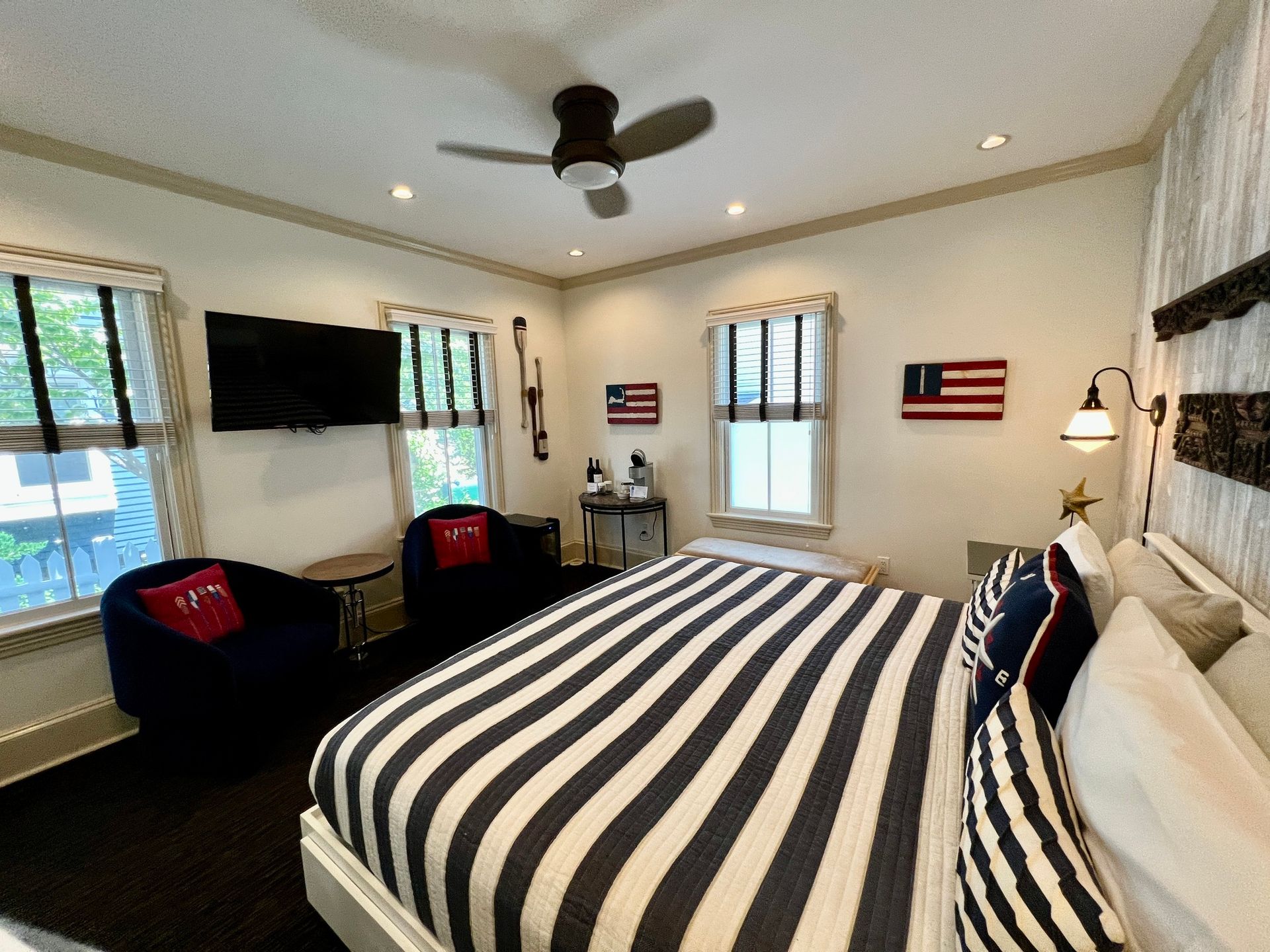 A bedroom with a king size bed , two chairs , a television and a ceiling fan.