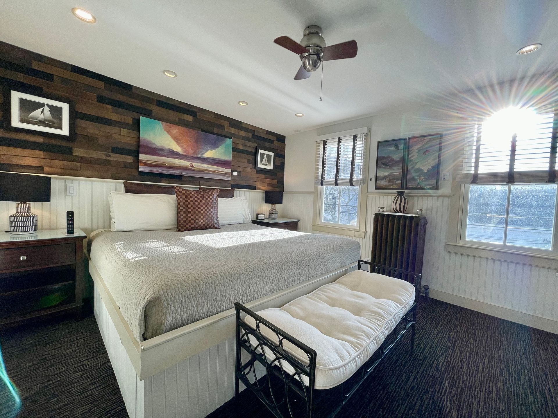 A bedroom with a king size bed , a bench and a ceiling fan.