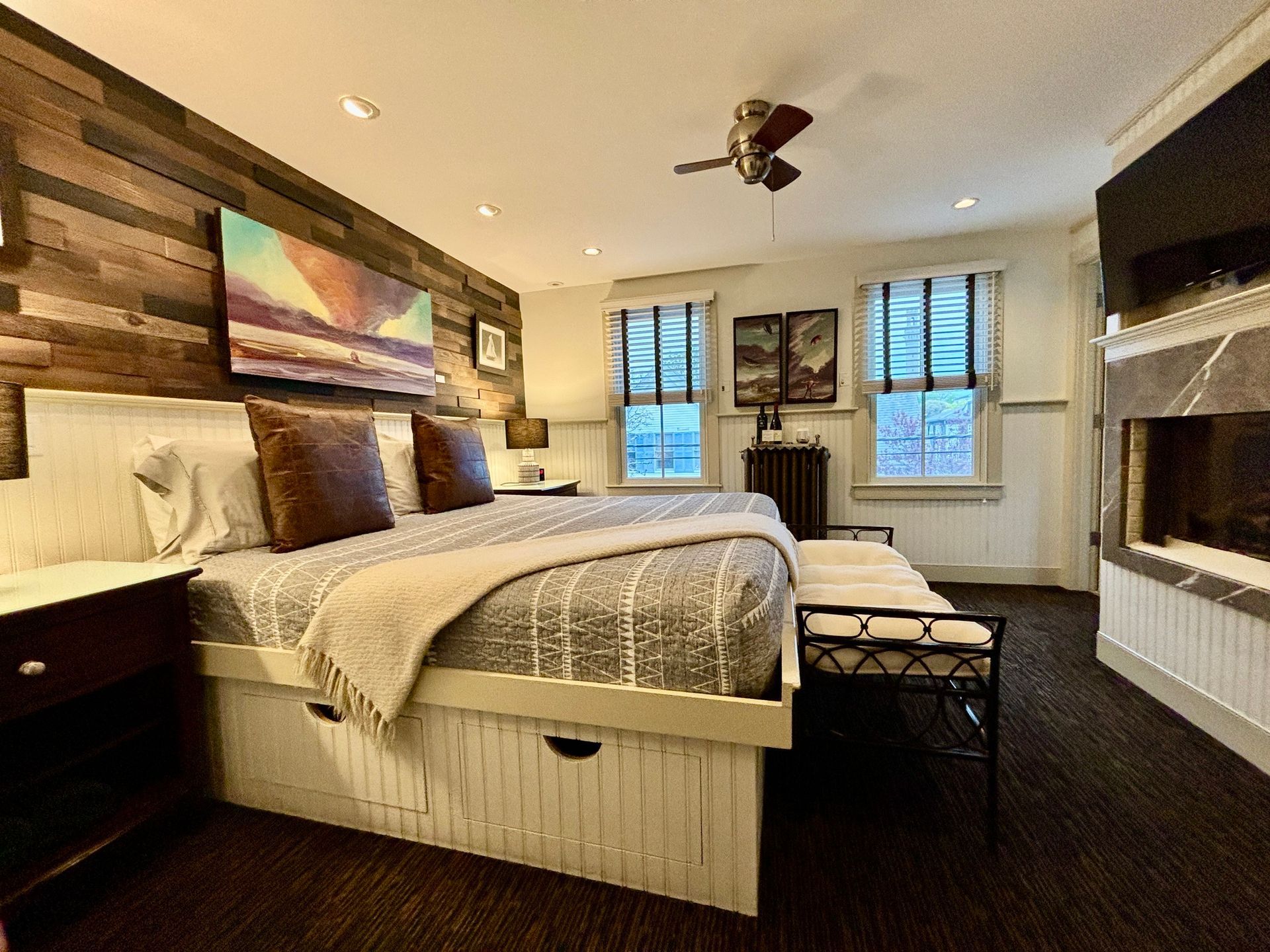 Interior guest room picture with king bed, wood textured wall two windows and a bench.