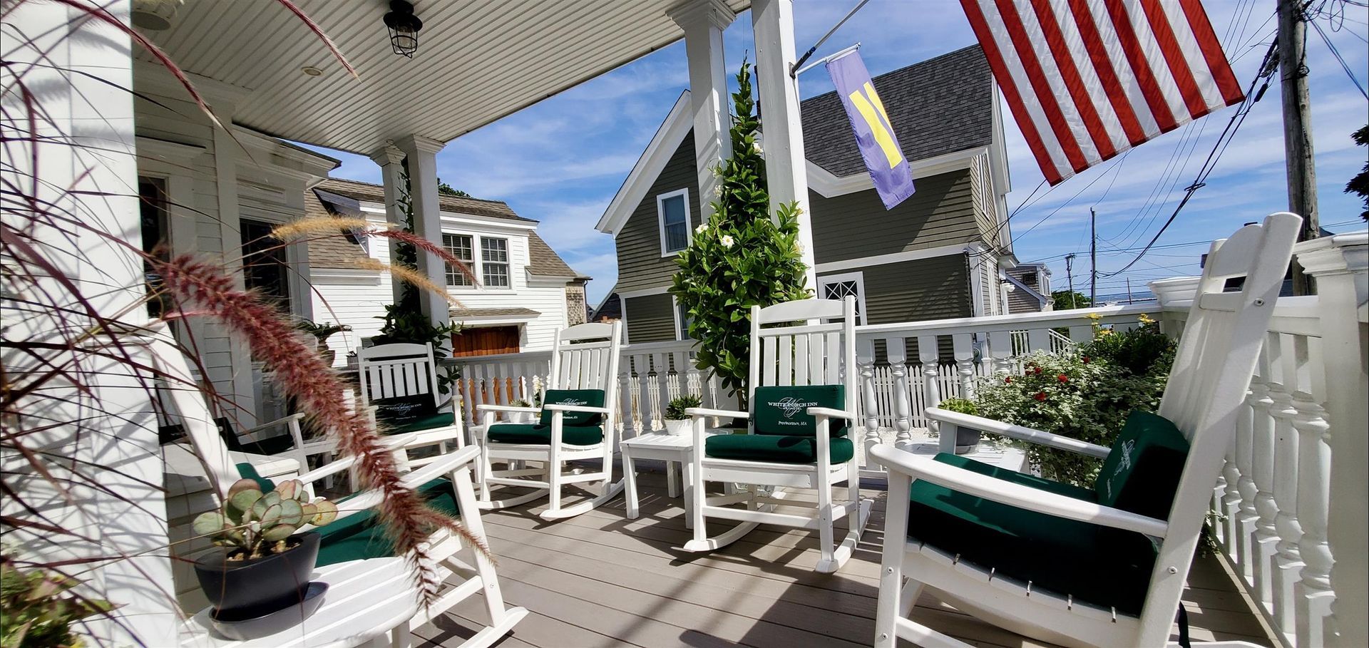 A black and white photo of a porch with rocking chairs and an american flag.