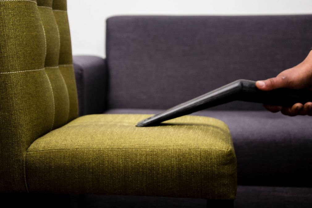 Hand holding a tablet above a green chair beside a gray sofa