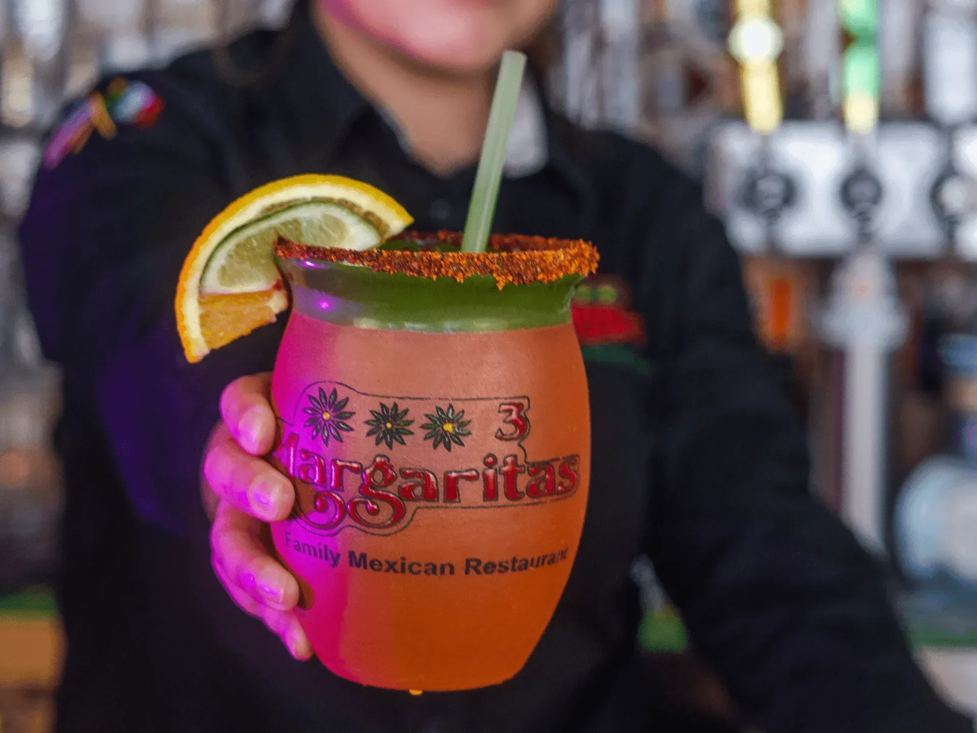 A woman is holding a margarita with a straw and a slice of lemon.