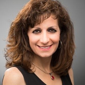 A woman wearing a black dress and a red necklace is smiling for the camera.