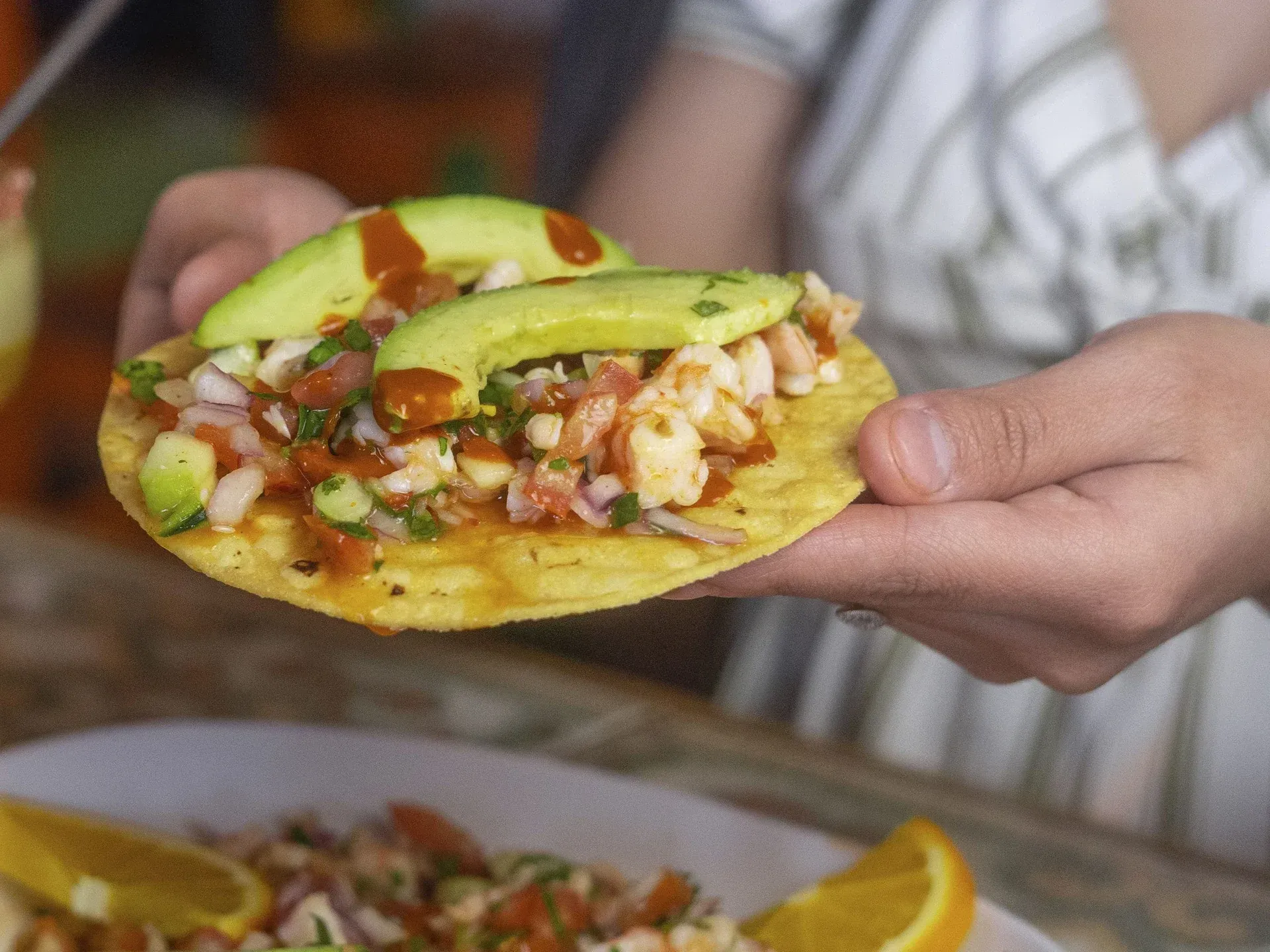 A person is holding a taco with avocado and shrimp on it.