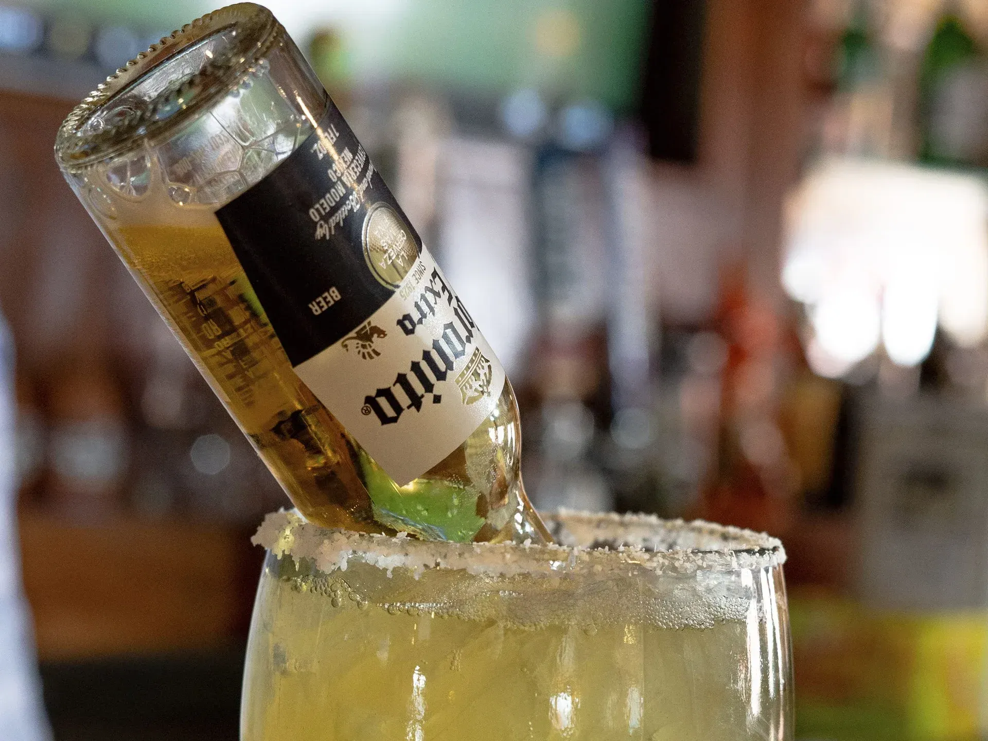 A bottle of corona beer is being poured into a margarita glass.