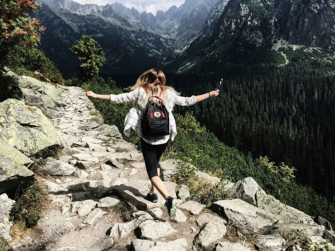 A woman with a backpack is walking up a rocky path in the mountains.