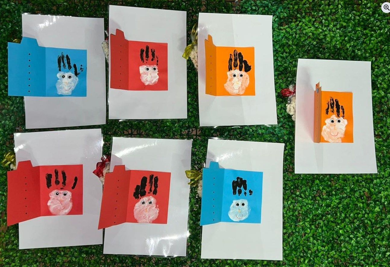 Handprint art cards in blue, orange, and red with white background and green grass.