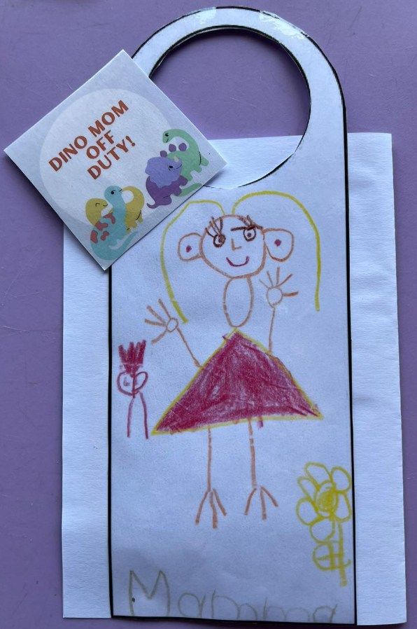 Child's drawing on a door hanger.  A stick figure with a red dress waves. 