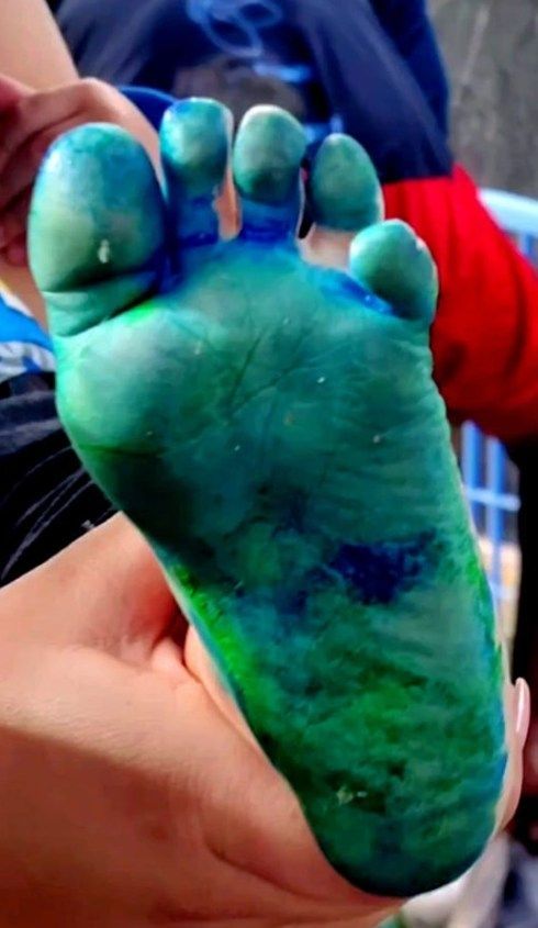 A foot covered in blue and green paint, held by a person.