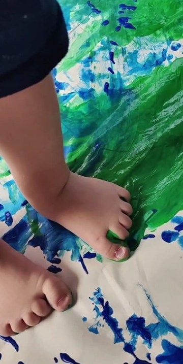 Child's feet walking on paper covered with blue and green paint.