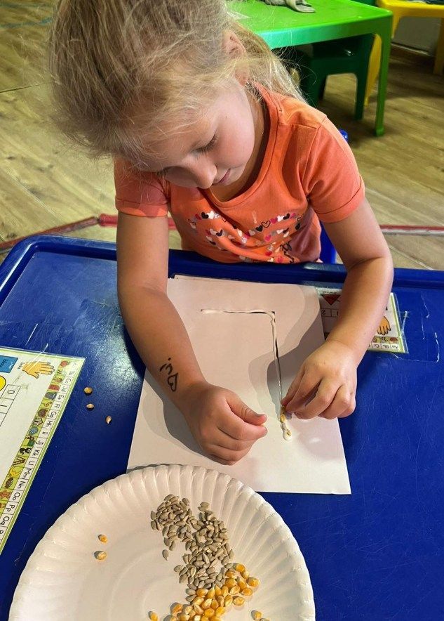 Young child placing seeds on paper at a table. Seeds on a plate.