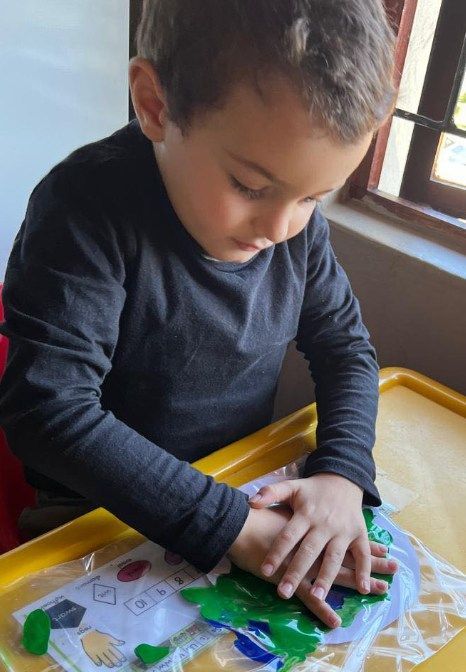 Boy pressing hands on a colorful educational activity, possibly a map, at a table near a window.