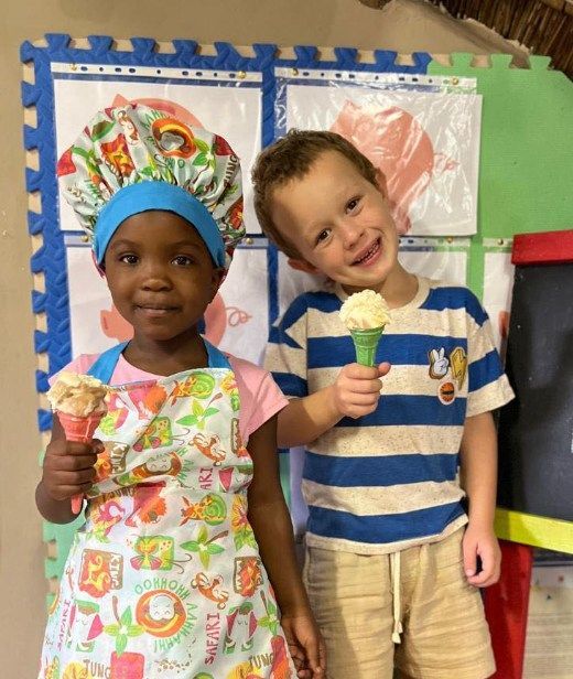 Two children hold ice cream cones, one wearing a chef hat and apron.