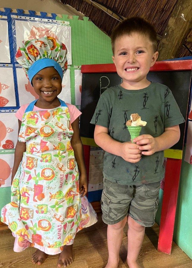 Two children smiling, one wearing a chef hat and apron, the other holding an ice cream cone.